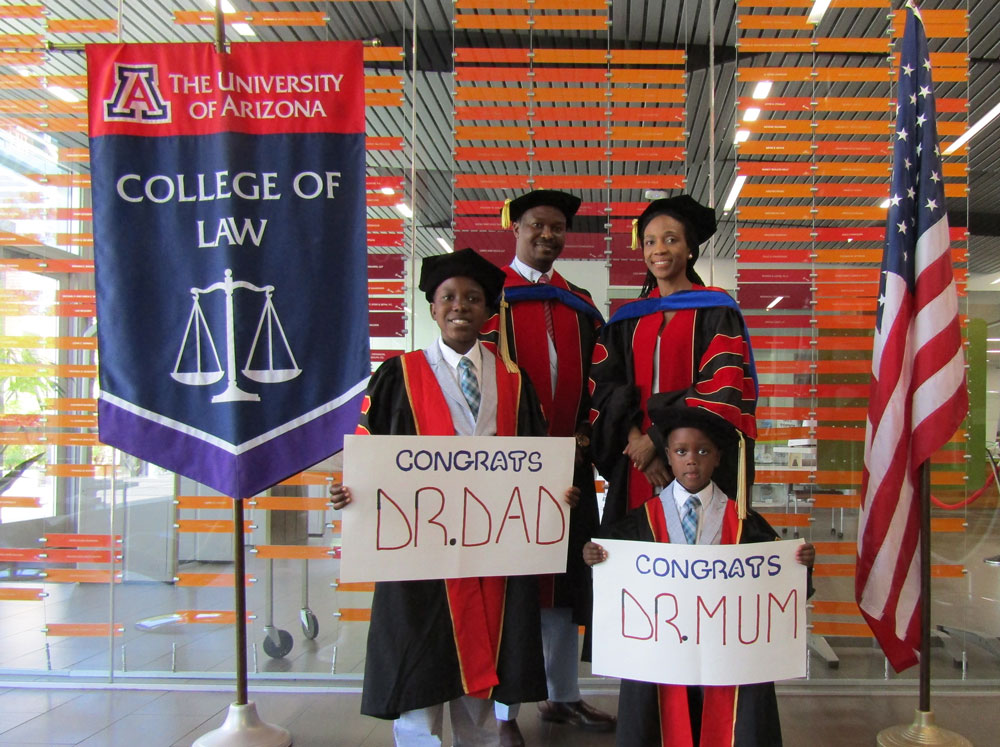 family in graduation robes with children holding "congrats" signs