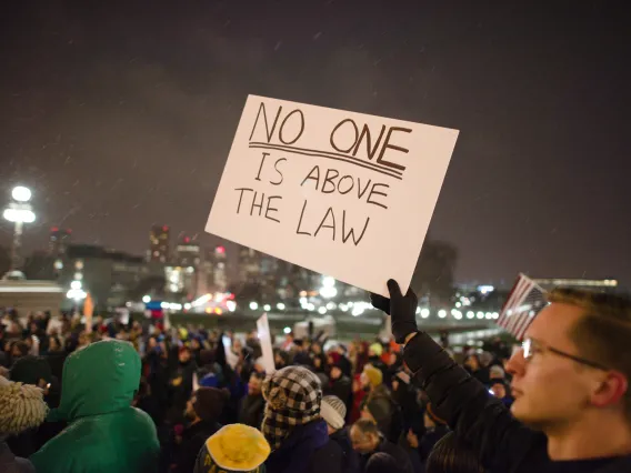 Protester in a crowd holding a sign that reads "No one is above the law" to protest President Donald Trump asking Attorney General Jeff Sessions to resign