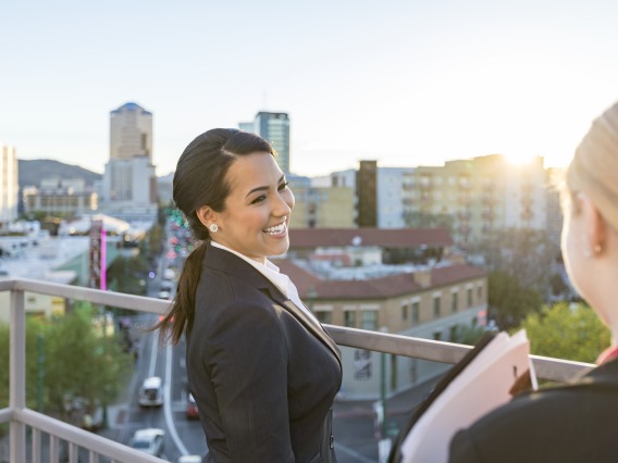 Two women in blazers chat on a balcony overlooking downtown Tucson.