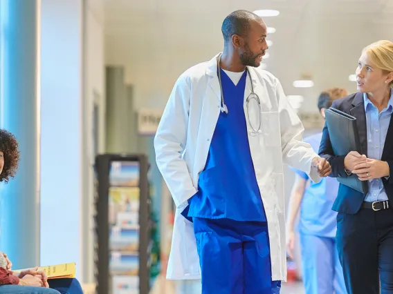 Male doctor in scrubs and a female hospital administrator in a suit talk in a hospital hallway