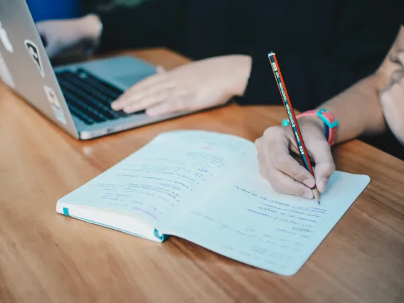 person on laptop and person taking notes in notepad