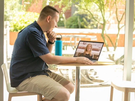A man sits at an outdoor table working on a laptop computer