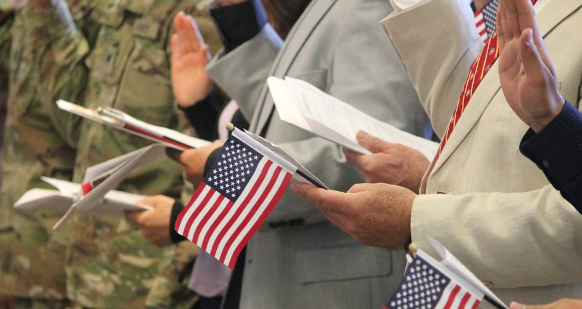 People raise their hands and hold U.S. flags at a U.S. citizen naturalization ceremony