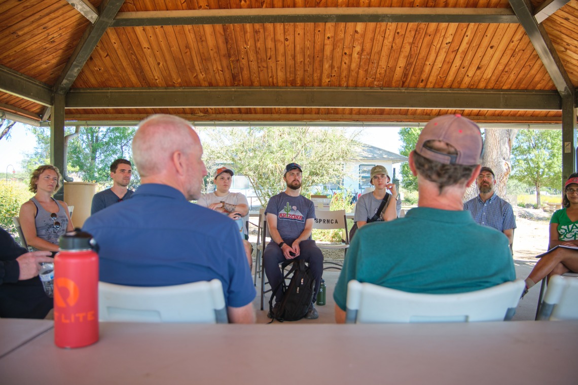 Natural Resource Clinic students listen to a presentation under a wooden pergola.