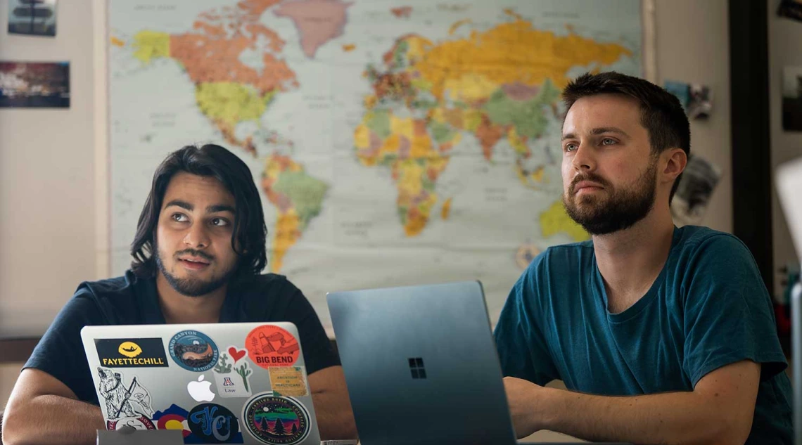 Two students learning, global map behind them