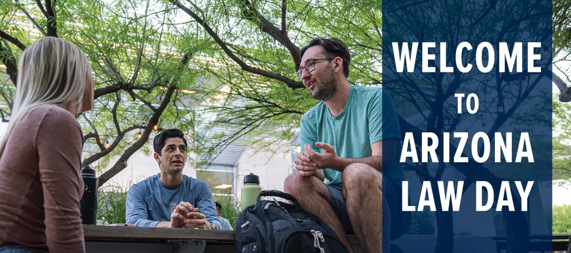 three students, one female and two male, sitting at picnic table under mesquite trees in Arizona Law courtyard