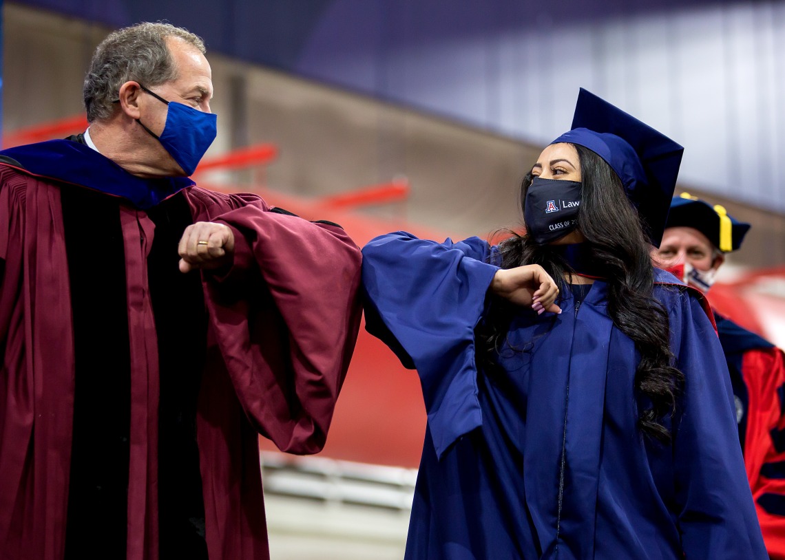 Bachelor's graduate in mask bumps elbows with Dean, also in mask, to celebrate graduation