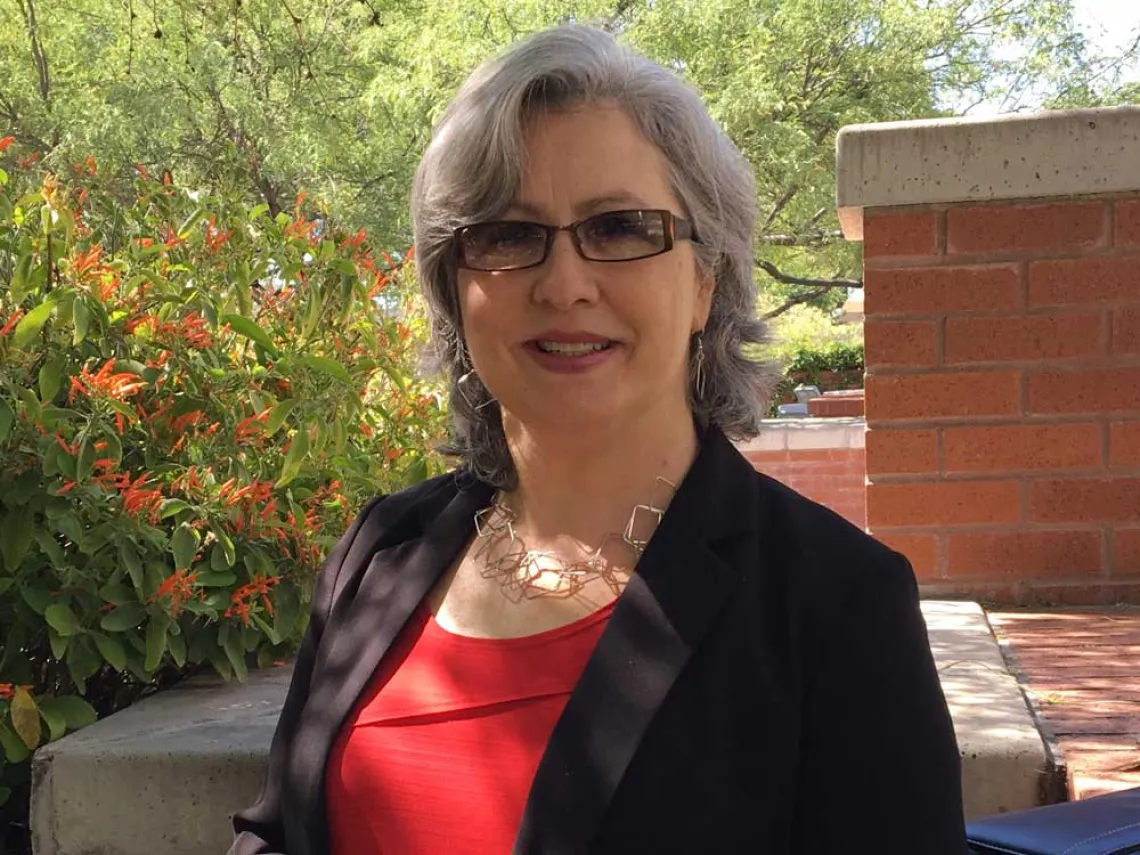 A woman in glasses and a blazer stands in a courtyard