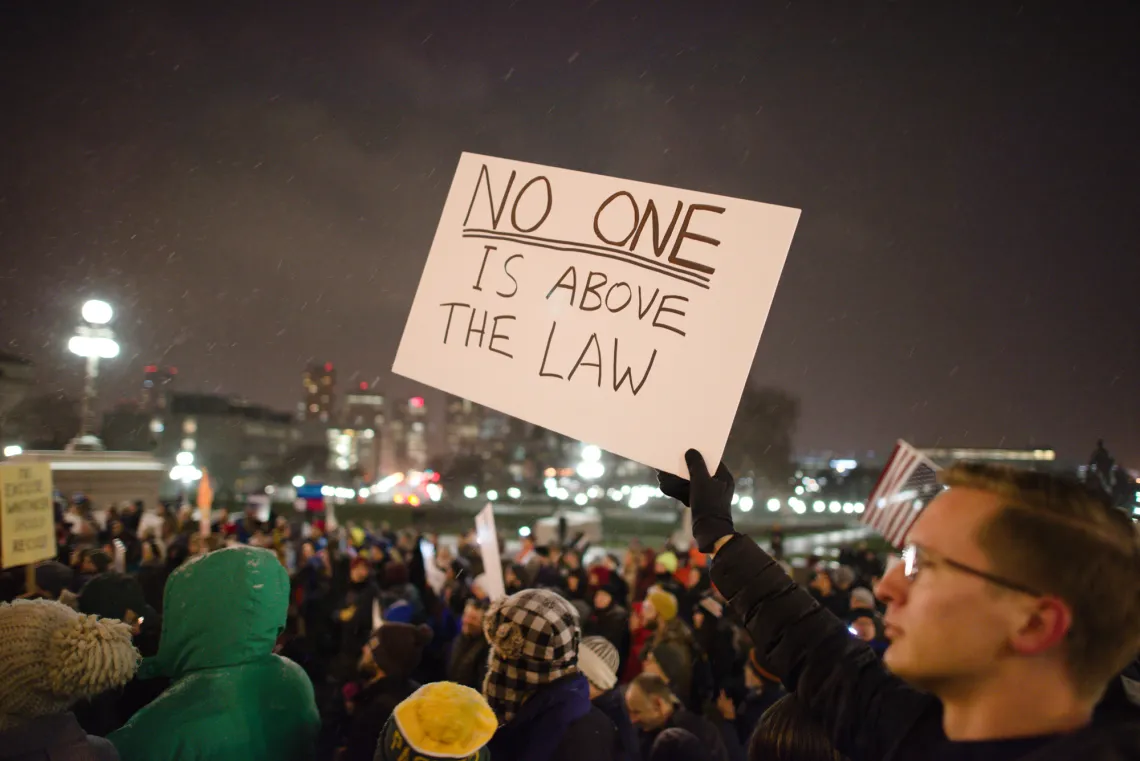 Protester in a crowd holding a sign that reads "No one is above the law" to protest President Donald Trump asking Attorney General Jeff Sessions to resign