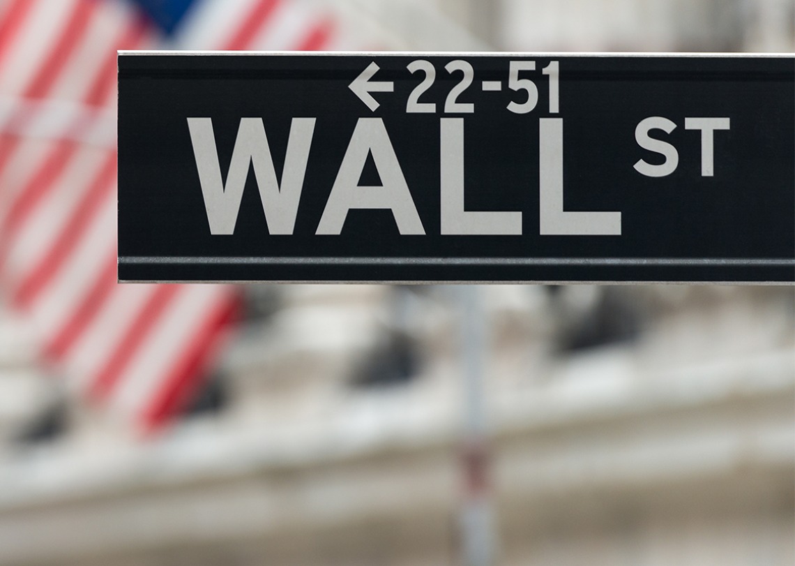 Wall Street street sign in front of American flags displayed on a building