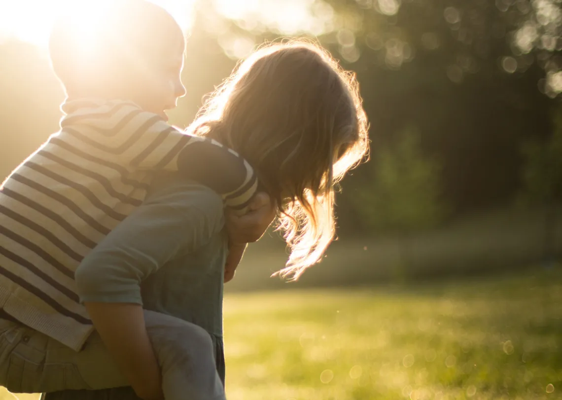 Woman carrying young child on her back in a grassy field