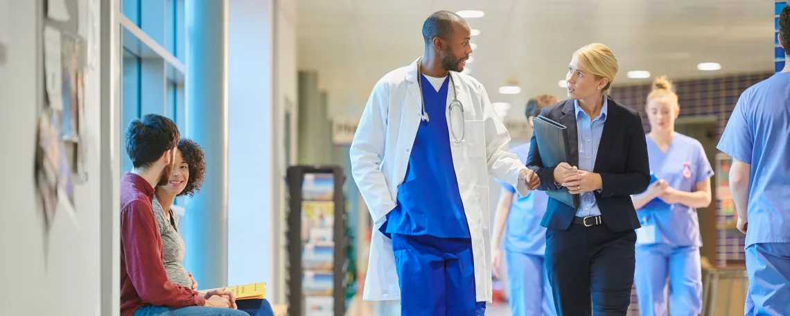 Male doctor in scrubs and a female hospital administrator in a suit talk in a hospital hallway