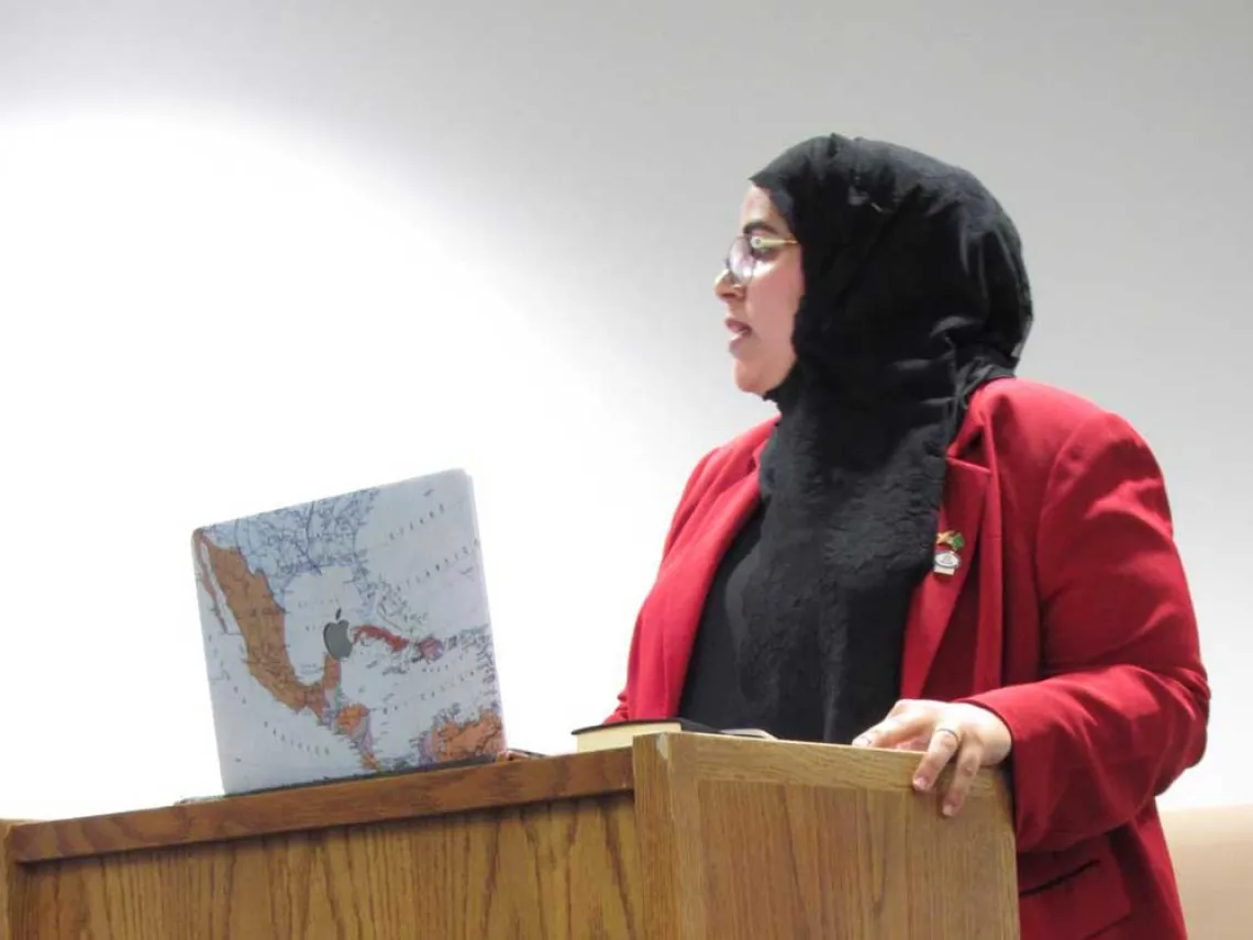 A woman stands at a podium with her laptop, giving a presentation