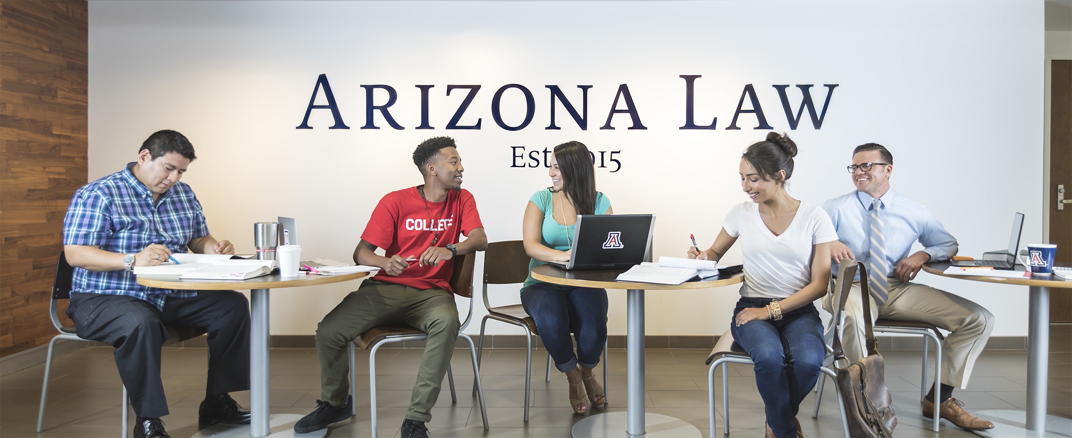 Five students study and talk while seated at tables in front of an Arizona Law sign