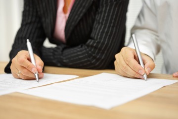Two people in business attire sign paperwork